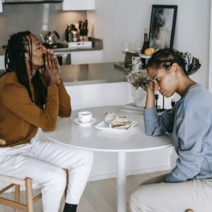 Young African American man sitting at table with woman and looking down thoughtfully while having conflict